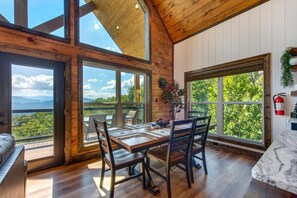 A dining area with a wooden table and chairs, large windows with a view of greenery and mountains, and a wooden ceiling. - Black Bear-y Ridge (Sevierville)