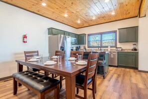 A dining area with a wooden table and chairs, a kitchen with green cabinets, and a fire extinguisher on the wall. - Hochatime (Sevierville)