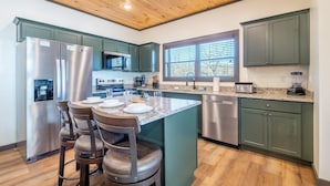 A kitchen with a central island, stainless steel appliances, and green cabinetry. - Hochatime (Sevierville)