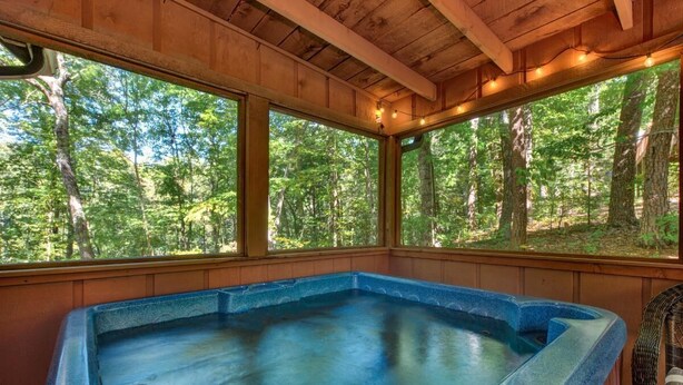 A hot tub in a wooden cabin with large windows overlooking a forest. - Whistling Woods Hideaway (Sevierville)