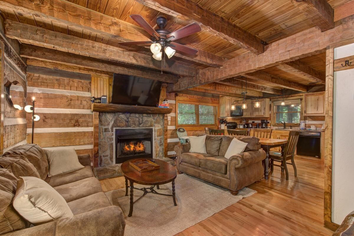 A rustic cabin interior with a stone fireplace, wooden furniture, and a kitchen area.