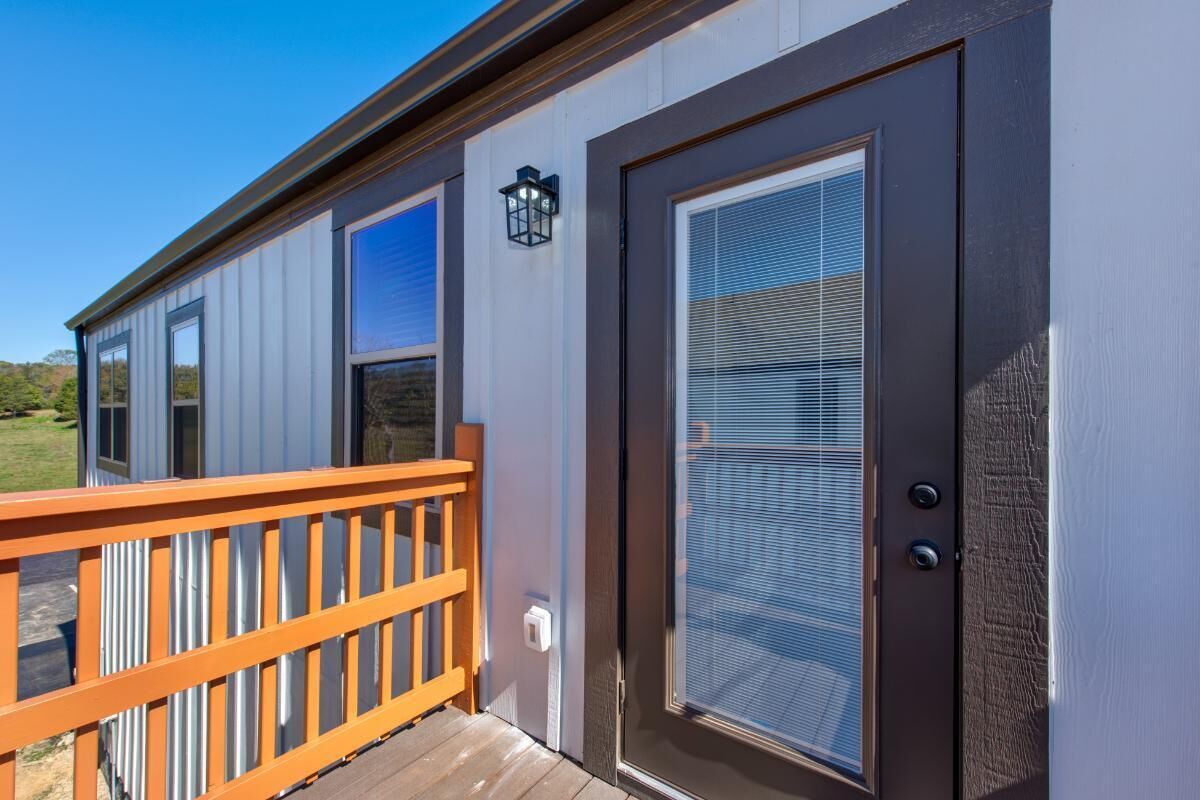 A single-story building with a wooden deck, a sliding glass door with a window, and a small outdoor light fixture.