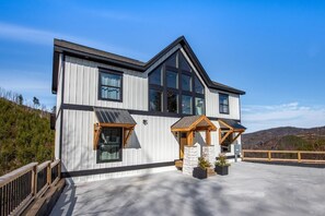 Ein modernes, zweistöckiges Haus mit großen Fenstern, einer Holzterrasse und einer Steineinfassung im Vordergrund.