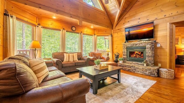 Ein gemütliches Blockhaus-Interieur mit Kamin, Ledersofas, einem Fernseher und großen Fenstern.