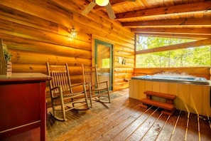 A wooden cabin interior with a hot tub, rocking chairs, and a wooden floor. - Smoky Breeze Retreat (Sevierville)