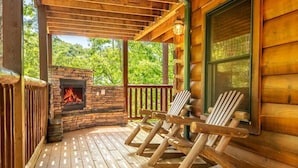 Eine Holzterrasse mit einem Kamin aus Stein und zwei Adirondack-Stühlen.