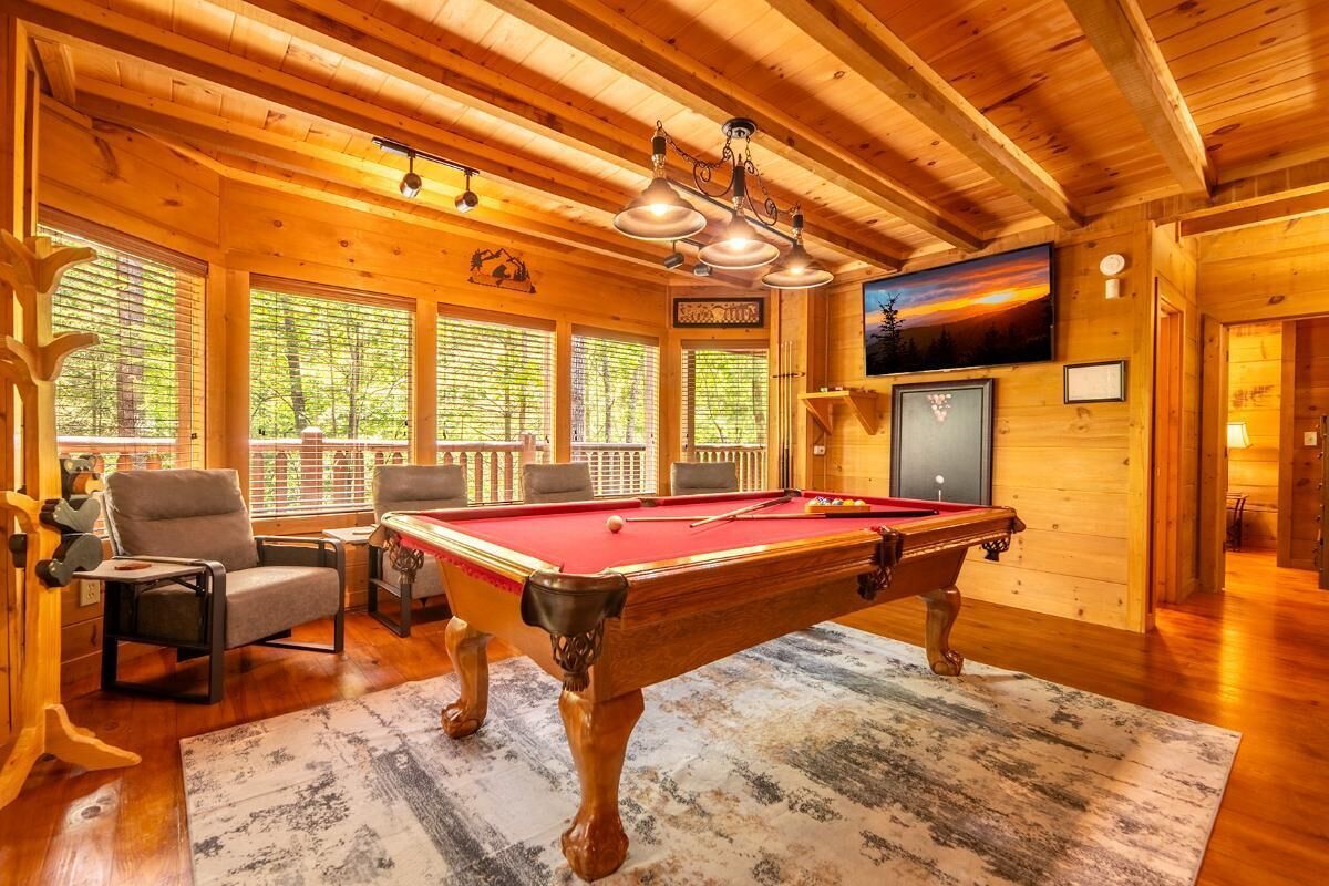 A wooden interior with a pool table, chairs, and a TV mounted on the wall.