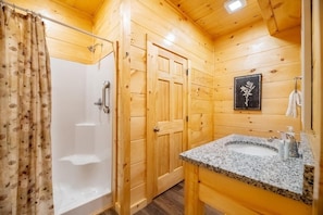 A wooden cabin bathroom with a shower, a sink, and a framed picture on the wall. - Z - Enchanted Pines (Pigeon Forge)