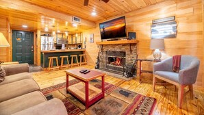 A cozy cabin interior with a fireplace, wooden floors, a TV, and a bar area. - Z - Black Bear Hideout (Gatlinburg)
