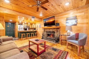 Ein gemütliches Blockhaus-Interieur mit Kamin, Holzböden, Fernseher und einer Bar.