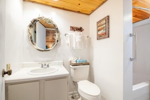 Ein Badezimmer mit Holzboden, einem runden Spiegel, einem weißen Waschbecken, einer Toilette und einem Handtuchhalter.