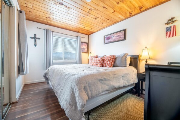 A bedroom with a bed, a nightstand, a lamp, a cross on the wall, and an American flag. - Mountain View (Gatlinburg)