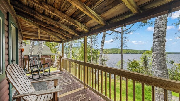 A wooden deck with Adirondack chairs, a wooden railing, and a view of a lake and trees. - NEW LISTING SPECIAL! Rangeley Lake | Shared Dock | Pet Friendly (Rangeley)