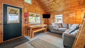 A log cabin interior with a wooden ceiling, a sofa, a table, and a television mounted on the wall. - NEW LISTING SPECIAL! Rangeley Lake | Shared Dock | Pet Friendly (Rangeley)