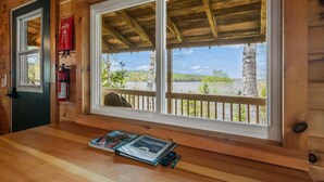 A wooden cabin with a wooden table, a magazine, a fire extinguisher, and a window with a view of trees and a dock. - NEW LISTING SPECIAL! Rangeley Lake | Shared Dock | Pet Friendly (Rangeley)