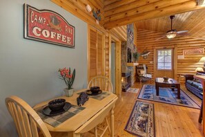 A cozy cabin interior with a dining table, chairs, a coffee table, a sofa, and a ceiling fan. - Unforgettable Dreams (Sevierville)