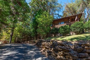 A cabin with a stone wall and a flag, surrounded by trees. - Unforgettable Dreams (Sevierville)