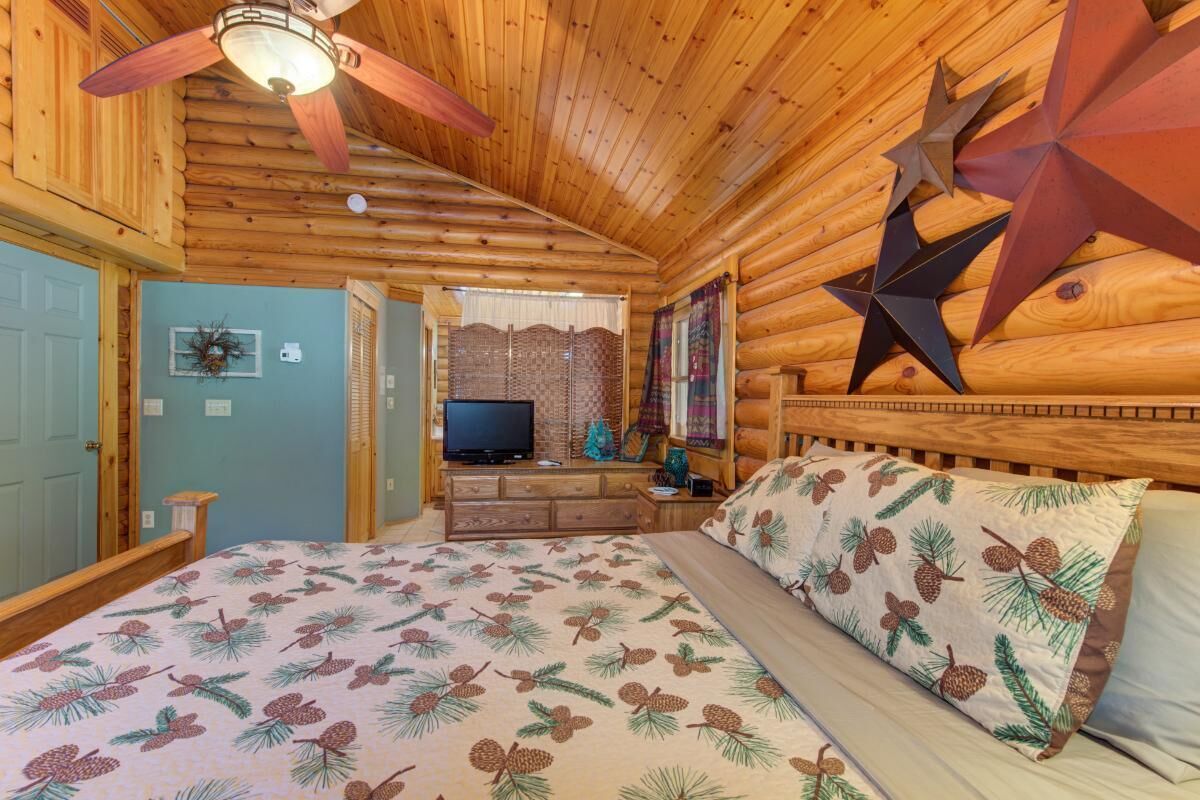 Un dormitorio tipo cabaña de madera con una cama, un ventilador de techo, decoración de estrellas, un televisor y una ventana pequeña.
