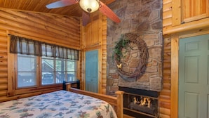 A log cabin interior with a bed, stone fireplace, and wooden walls. - Unforgettable Dreams (Sevierville)