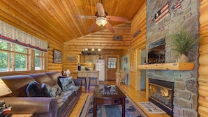 A log cabin interior with a fireplace, wooden ceiling, and a sofa in the living area. - Unforgettable Dreams (Sevierville)