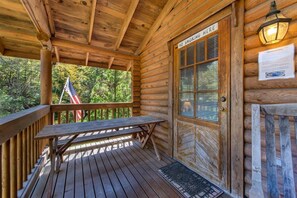 A wooden cabin with a covered porch, a bench, a door with a 'No Smoking Here' sign, and an American flag. - Unforgettable Dreams (Sevierville)
