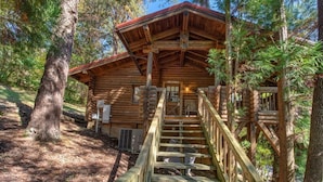 A log cabin with a wooden staircase leading to a porch, surrounded by trees. - Unforgettable Dreams (Sevierville)