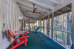 A covered porch with a ceiling fan, red Adirondack chairs, a small table with a glass top, and a view of trees through large windows. - Z - Clear Fork Farm (Sevierville)