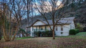 Ein Haus mit Veranda, einem kleinen Garten und Blick auf ein bewaldetes Gebiet.
