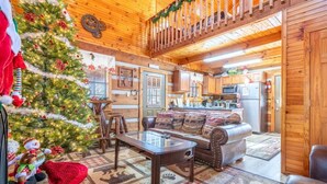 A cozy cabin interior with a Christmas tree, wooden walls, a dining area, and a kitchen. - Antlers Haven (Pigeon Forge)
