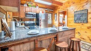 A wooden lodge kitchen with granite countertops, stainless steel appliances, and a bar area with stools. - Antlers Haven (Pigeon Forge)