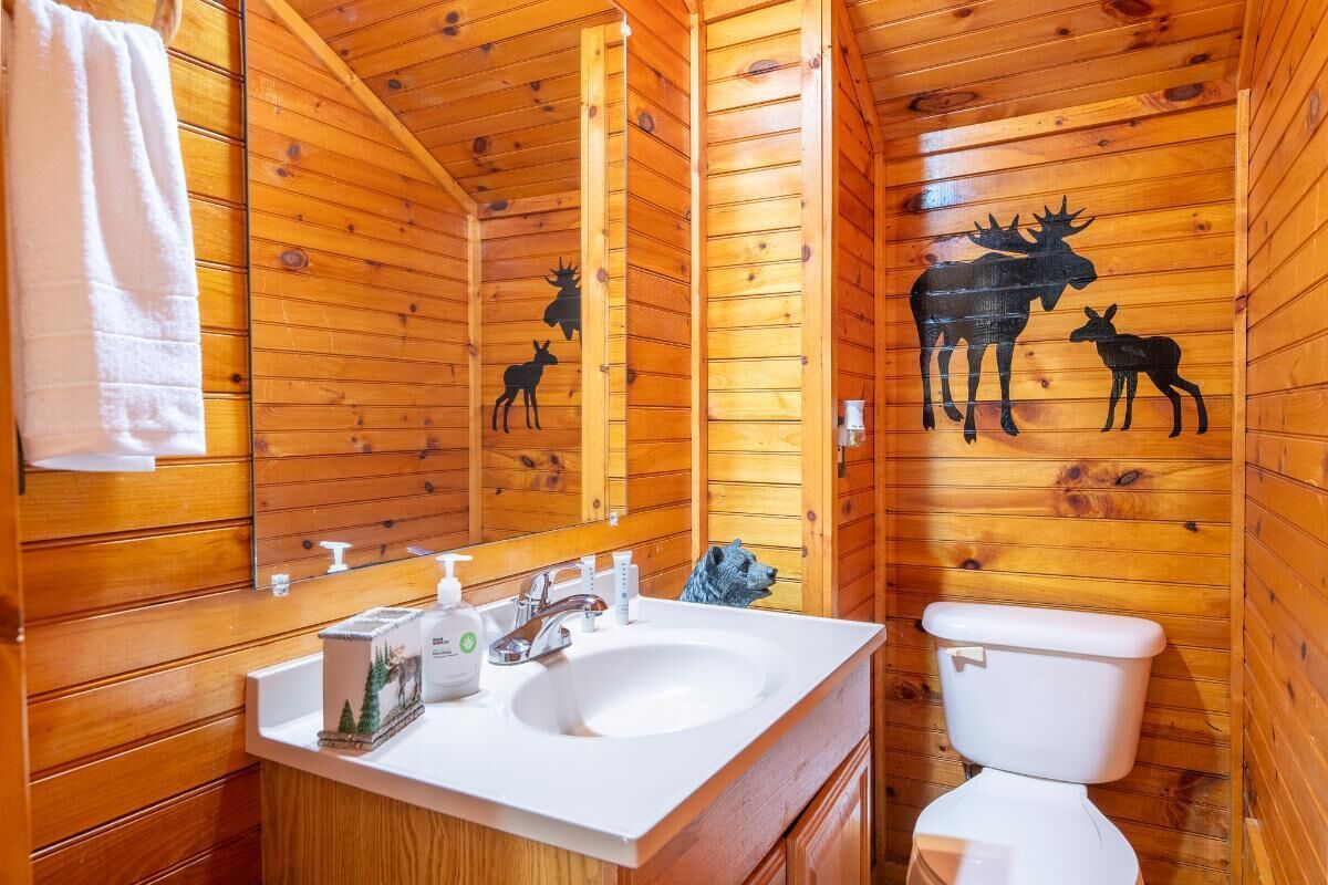 Ein Badezimmer einer Holzhütte mit Waschbecken, Toilette und Wandbild eines Elchs.