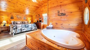 A log cabin room with a bed, a wooden floor, a hot tub, and a window. - Antlers Haven (Pigeon Forge)
