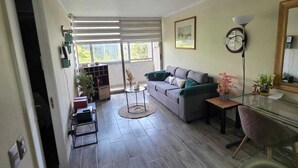 Ett vardagsrum med en soffa, ett soffbord, en lampa och utsikt genom en skjutdörr till en balkong.
