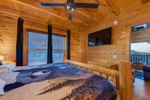 A wooden cabin room with a bed, a ceiling fan, a mounted TV, and a window with blinds. - Z - Tennessee Whiskey (Sevierville)