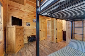 A wooden cabin interior with a bunk bed, a TV, a dresser, and a door leading to another room. - Rustic Modern Mountain Cabin (Pigeon Forge)