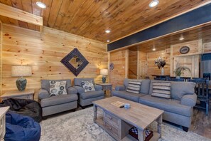 A cozy living room with wooden walls, two grey sofas, a coffee table, and a blue bean bag. - Rustic Modern Mountain Cabin (Pigeon Forge)