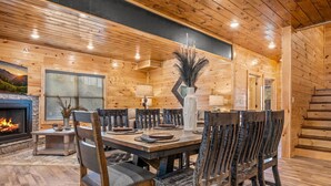 A wooden-paneled dining room with a fireplace, a table set for six, and a large vase with dried plants. - Rustic Modern Mountain Cabin (Pigeon Forge)