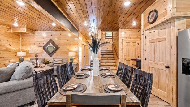 A wooden interior with a dining table set for six, surrounded by chairs, a sofa, and a refrigerator. - Rustic Modern Mountain Cabin (Pigeon Forge)