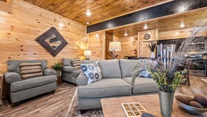 A cozy living room with wooden walls, a gray sofa, and a coffee table with decorative items. - Rustic Modern Mountain Cabin (Pigeon Forge)