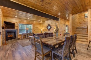 A wooden interior with a fireplace, dining table, and chairs. - Rustic Modern Mountain Cabin (Pigeon Forge)