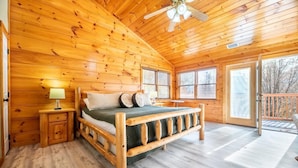 Camera da letto in una baita di legno con un letto, un comodino e vista sull'esterno.