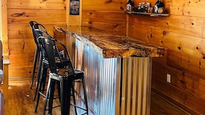 Angolo bar con pareti in legno, un bancone in metallo e sgabelli da bar neri.