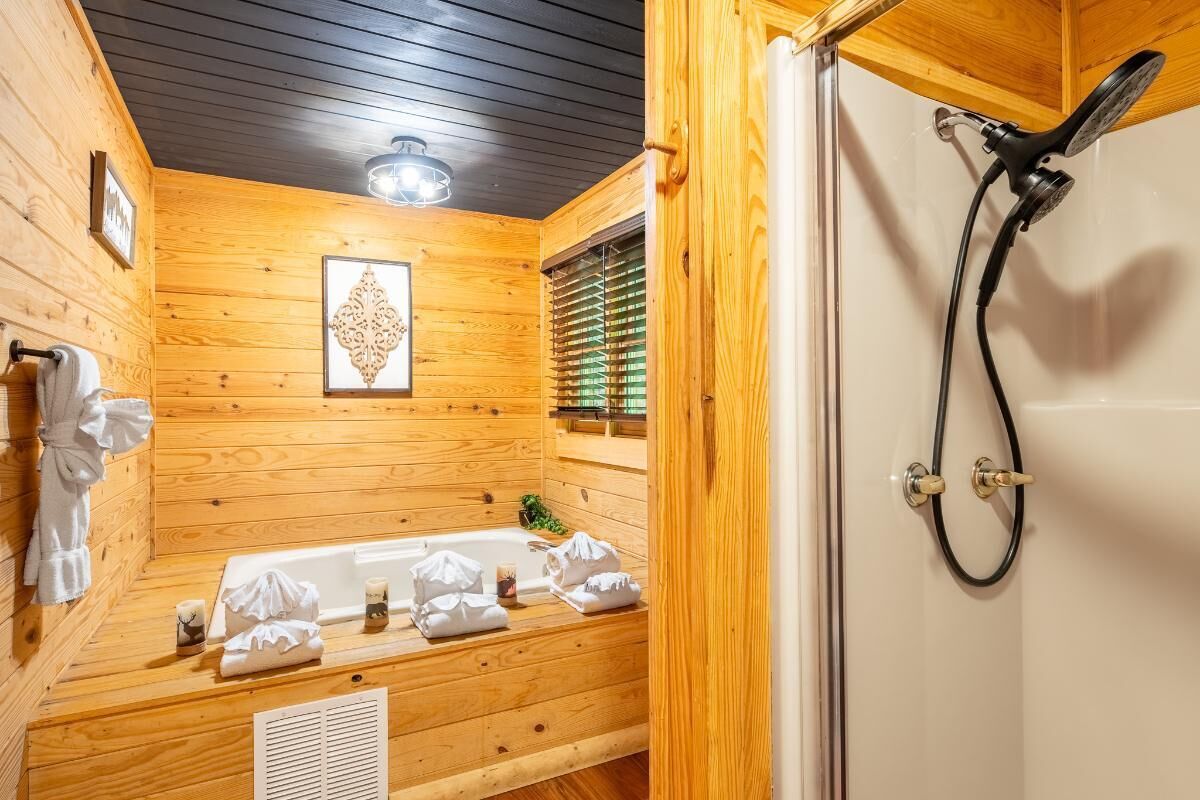 A wooden cabin bathroom with a bathtub, shower, and a window with blinds.