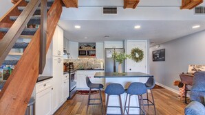 Una cocina moderna con armarios blancos, una escalera de madera y una zona de bar con taburetes.