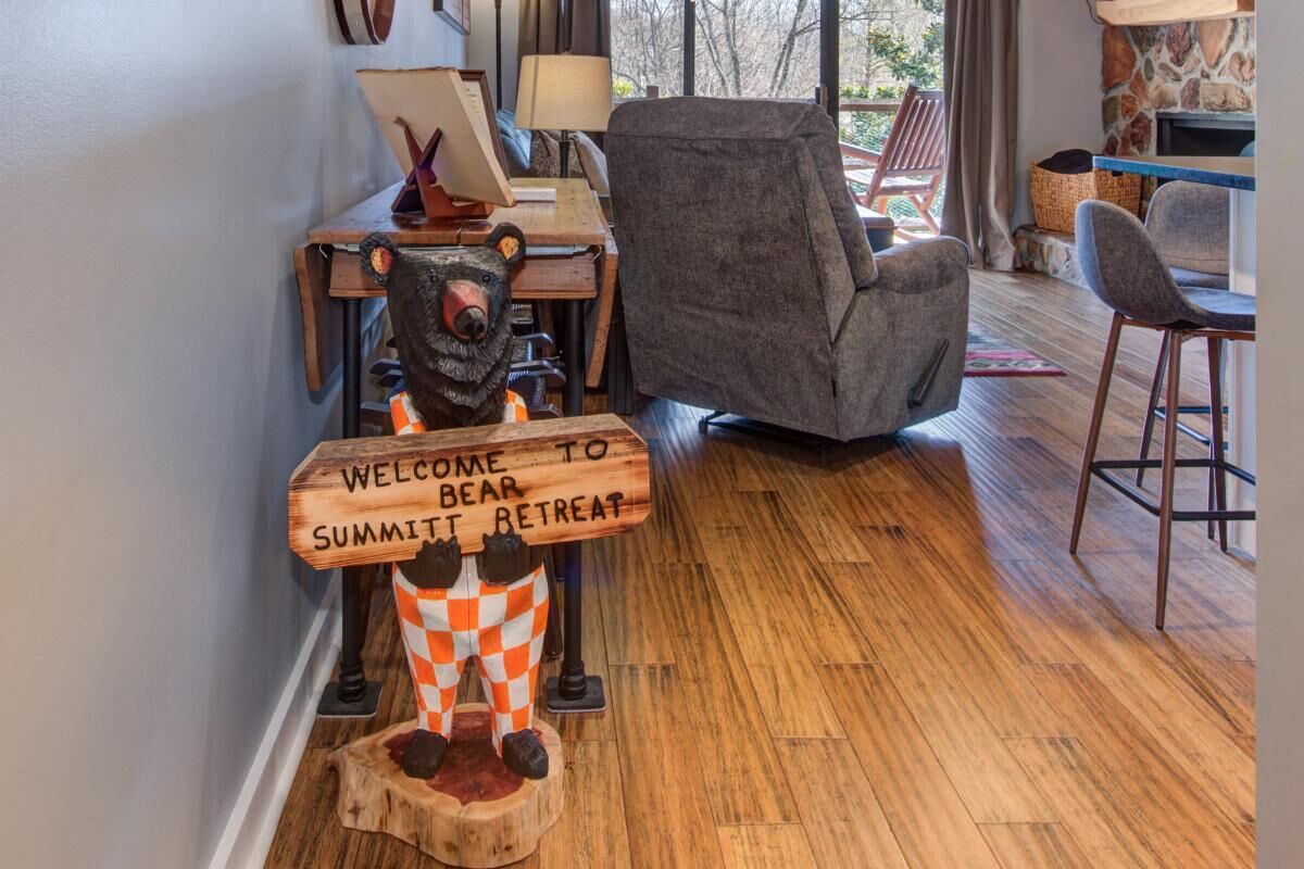 A wooden sign with a bear figure, a gray armchair, and a wooden floor.