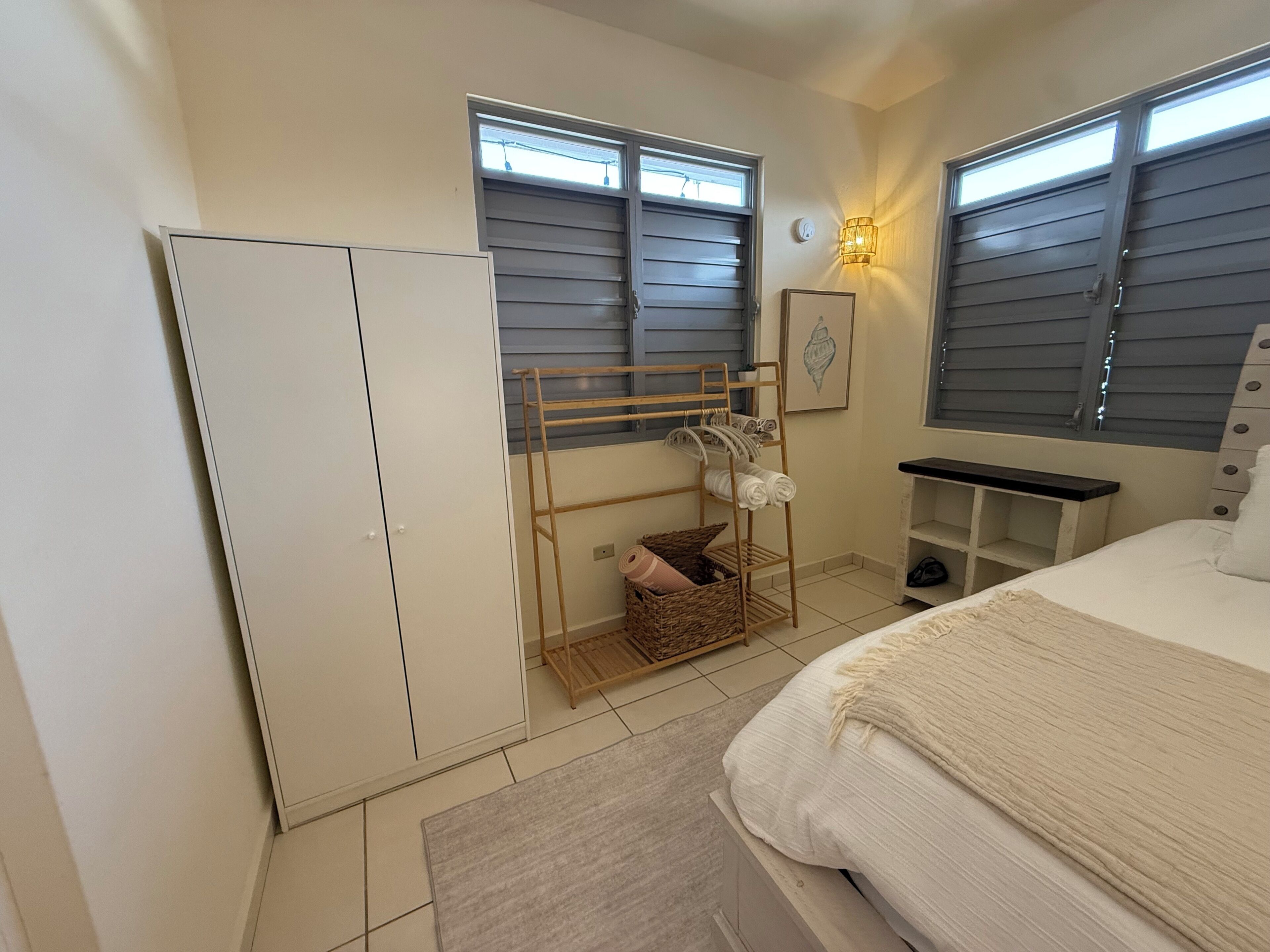 Een slaapkamer met een bed, een kledingkast, een droogrek en een klein plankje.