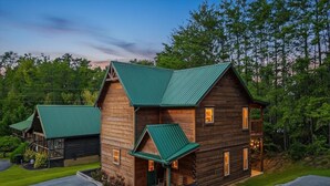 A log cabin with a green roof, a porch, and a small attached structure. - Mountain Getaway (Pigeon Forge)