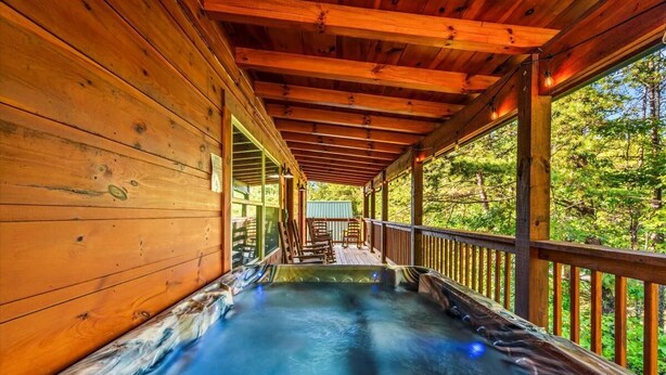 A wooden cabin with a hot tub and a deck overlooking a forest. - Mountain Getaway (Pigeon Forge)