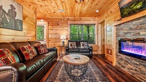 A cozy cabin interior with a leather sofa, a round coffee table, a fireplace, and a television mounted on the wall. - Mountain Getaway (Pigeon Forge)