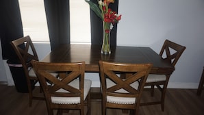A dining table with four wooden chairs, a vase with flowers, and a window with blinds. - Modern Heart of Hollywood (Hollywood)